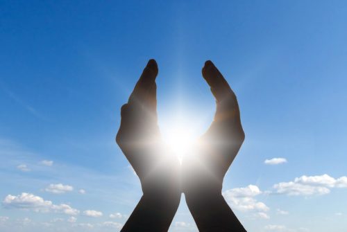 2 hands raised against sky with energy between them